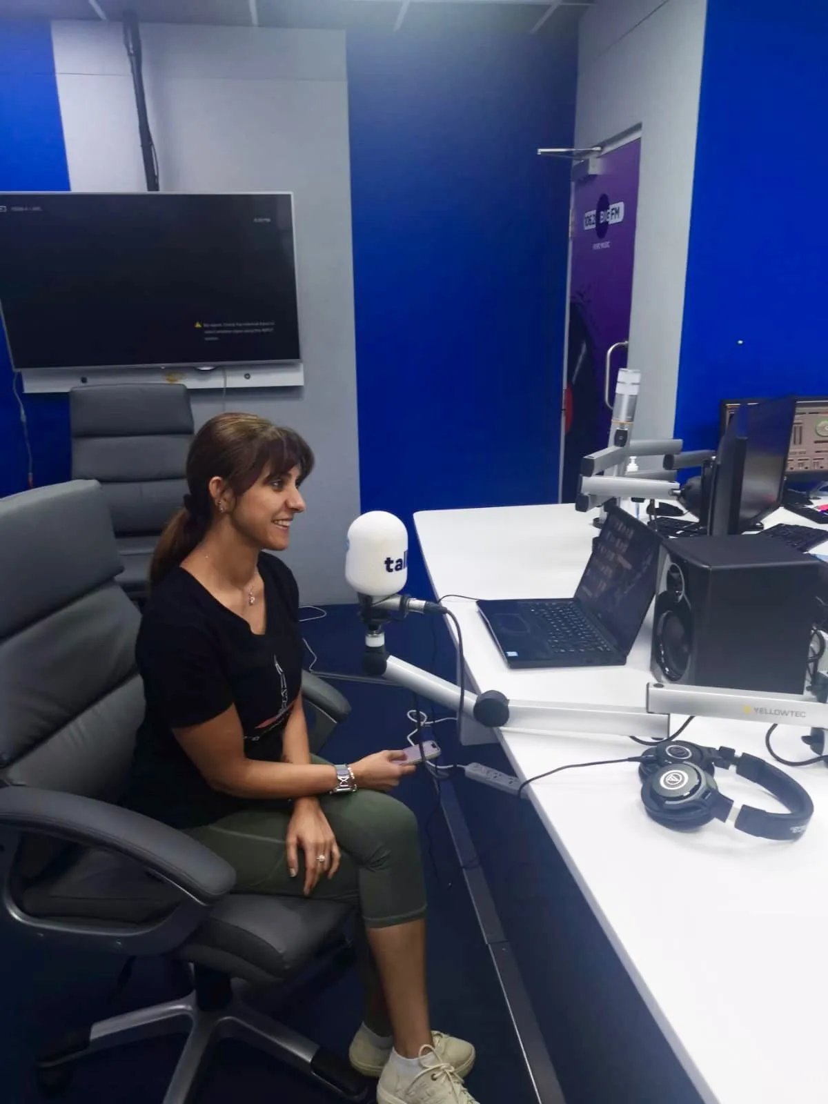 Brinda smiling at the microphone in the Talk 100.3 FM studio